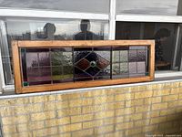 Panel leaning against exterior building wall showing wood frame and stained glass design