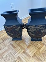 Front and side view of two square-shaped blue vases with gold dragon motifs and lion head handles on wooden parquet floor.