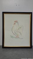 Full view of framed Picasso Rooster print on wall, showing black frame with gold trim and the colorful minimalist rooster artwork.