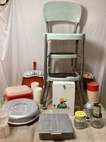 Full view of lot including step stool/chair, dustpans, aluminum bakeware, plastic cups, containers and jars placed on burlap fabric