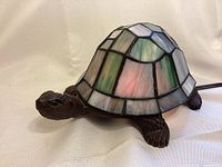 Side view of stained glass and metal turtle lamp showing the stained glass shell with metal framing and textured metal body.