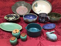 Overview of all pottery items including bowls, mug, bunny figurine, shakers, sugar bowl on red fabric background