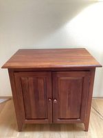 Front view of the solid wood cabinet showing two paneled doors with wooden knobs and tapered legs.