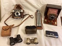Overview of the lot showing vintage cameras, binoculars, tripod, and cases on white background.
