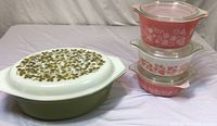 Olive green oval casserole and stack of three pink and white round casserole dishes with lids