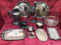 Full display of all vintage silver-plated serving pieces plus cut glass bowl and bird-themed salt and pepper shakers arranged on red brocade fabric