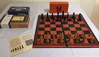 Vintage chess set displayed with wooden pieces arranged on a red and black folding chess board, alongside dominoes in a tin box, and several gift and stationery boxes.