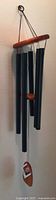 Full view of Woodstock Chimes wind chime with black metal tubes and wood parts, hung and visible in use.