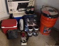 Full camping lot setup showing cooler boxes, camping stove box, propane tanks, lanterns, and emergency honey pots.