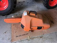 Chainsaw in closed orange hard-plastic case beside tractor tire