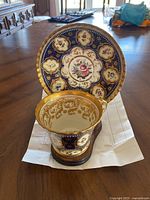 Photo showing teacup and saucer together from front angle on table, highlighting floral and gold designs
