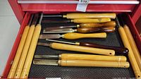 Drawer opened showing multiple woodworking chisels with wooden handles in various sizes and blade types.