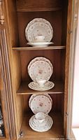 Full display of three place settings of Coalport china inside a cabinet, showing plates, bowls, teacups, and saucers arranged on shelves.