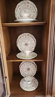 Three shelves each displaying a full place setting of Coalport china including plates, bowls, teacups, and saucers with floral pattern and gold trim.