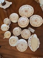 Full set laid out on wooden table showing stacks of 3 sizes of plates, multiple teacups and saucers, and a gravy boat with underplate