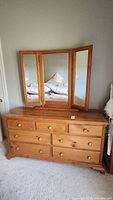 Full front view of the wooden dresser with tri-fold mirror showing nine drawers and round knobs.