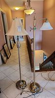 Full view of two metal floor lamps standing side by side showing different shade styles and heights.
