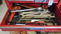 Drawer containing multiple wrenches and red-handled pliers and screwdrivers