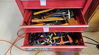 Two open drawers of red toolbox showing assorted hand tools