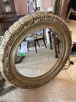 Full view of the round mirror showing decorative carved frame and stand on carpeted floor.