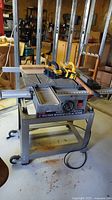 Front perspective view of table saw on stand showing sliding table, fence and clamps