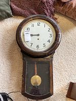 Front view of wall clock lying on carpet showing round wooden bezel and lower case