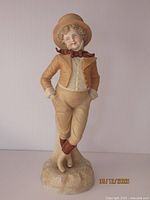 Front view of antique Rudolstadt bisque porcelain figurine of a young dandy, showing detailed facial features, clothing in beige and brown tones, and standing pose on base.