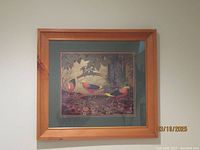 Framed print showing three golden pheasants among foliage. Double matted in beige and green, natural wood frame. Signed lower right.