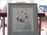 Full view of framed painting showing five angelfish swimming among plants in muted tones with green mat and wooden frame.