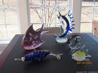 Five different art glass fish sculptures on table with window background