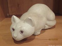 Front angled view of the white stone cat sculpture lying down, showing the glass eyes and facial features.