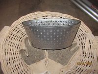 Wicker basket with a pair of beige garden gloves featuring black dots and a small perforated metal container inside.