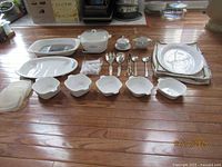 Full view of the set arranged on wooden floor, showing Corning Ware Blue Cornflower dishes, condiment dishes, serving utensils and plastic covers.
