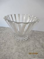 Clear crystal vessel with fluted scalloped rim and faceted base on marble surface.