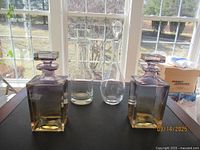 Two square-shaped crystal decanters with stoppers and two glass water ewers with stoppers displayed on a black surface with natural light.