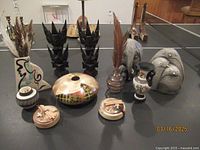 Multiple vintage and ethnic decorative items including pottery vases, carved wood figures, and elephant figurines arranged on black table.
