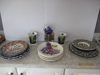 Photo of the full lot showing the plates stacked in groups, two Pimpernel mugs, Pimpernel coaster behind stem wine glass decorated with grapes