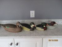 Four hand crafted wooden duck decoys lined up showing front and profile views and size scale