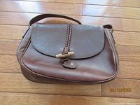Brown leather shoulder bag with toggle closure on wooden floor