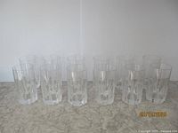 Twelve highball glasses arranged in two rows on a marble surface against a white background