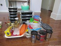 Photo showing assorted plastic containers, black plastic take out containers with lids stacked, orange plastic trays, stainless steel travel mugs, plastic pitcher, and other kitchen items.