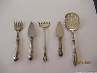 Five sterling silver utensils laid out on a plain background including forks, spreaders, and a spoon, showing their overall size and ornate handles.