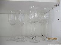 Seven crystal stem wine glasses arranged in a row on a shelf, three Waterford Marquis and four Lenox Tuscany Classics.
