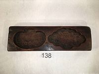 Top-down view of dark hardwood moon cake mold with two carved cavities, left cavity with mushroom shape and right cavity with lotus flower in bloom shape.