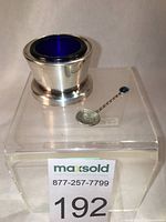Silver-plated open salt cellar with cobalt glass liner and New Zealand coin spoon placed on clear plastic stand
