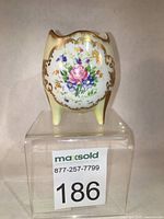 Front view showing floral decal with pink rose and blue flowers, gold scallops on creamy porcelain with three legs.