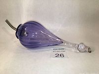 Side angle view showing the purple glass body with ripple texture, clear spout, and hanging knob top.