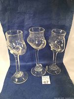 Three hand blown glass goblets displayed against a blue fabric background showing their unique bulbous shapes and stems.