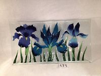 Full view of fused art glass plate with three blue iris flowers and green foliage on a clear textured background.