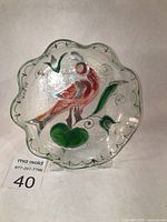 Fused glass plate with scalloped edges, featuring hand-painted stylized bird and leaf design. View shows front of plate, signed 'SLAVA' on side and silver or platinum accents on scalloped edge, frosted glass exterior.